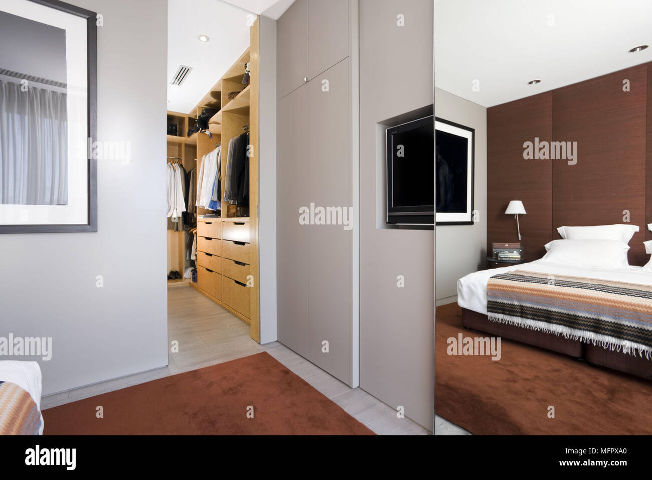 Sliding mirrored door concealing television and fitted wardrobes in modern bedroom with adjoining dressing room Stock Photo