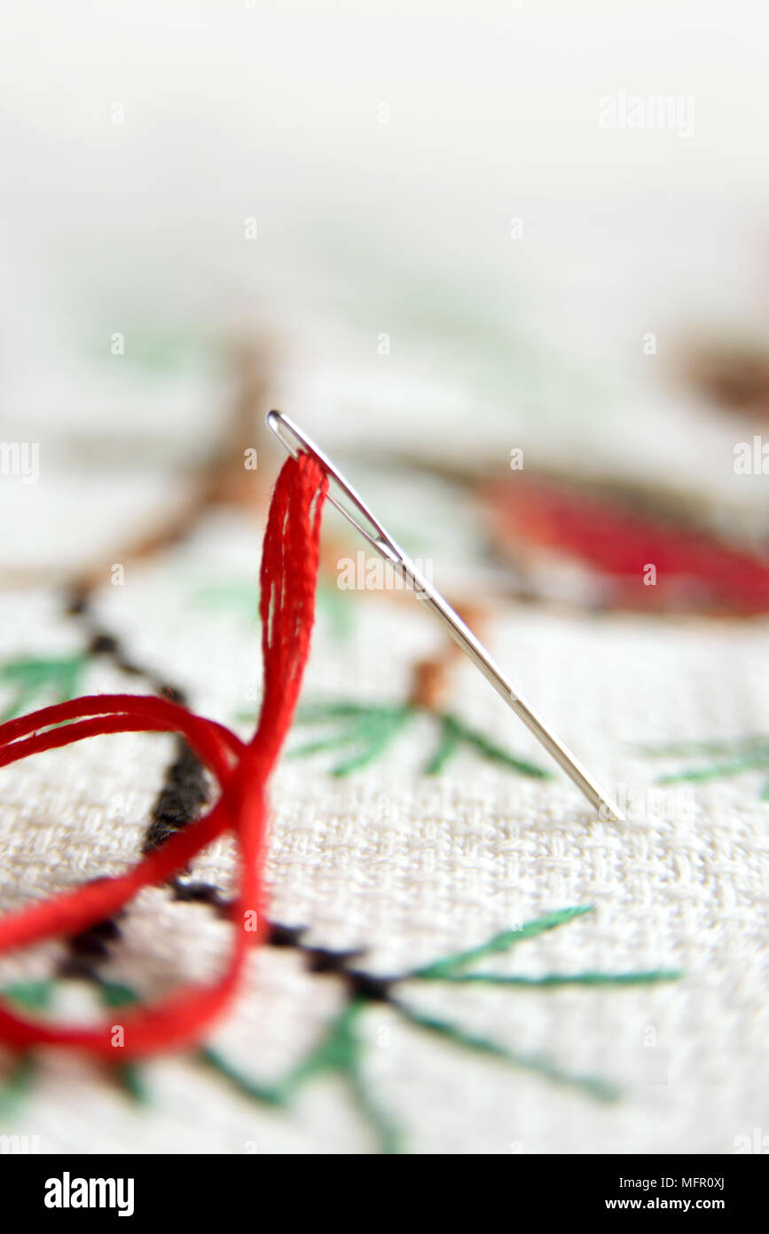 Cross-stitch embroidery and needle with red thread. Embroidery macro close up. View from above. Free copy space. Stock Photo