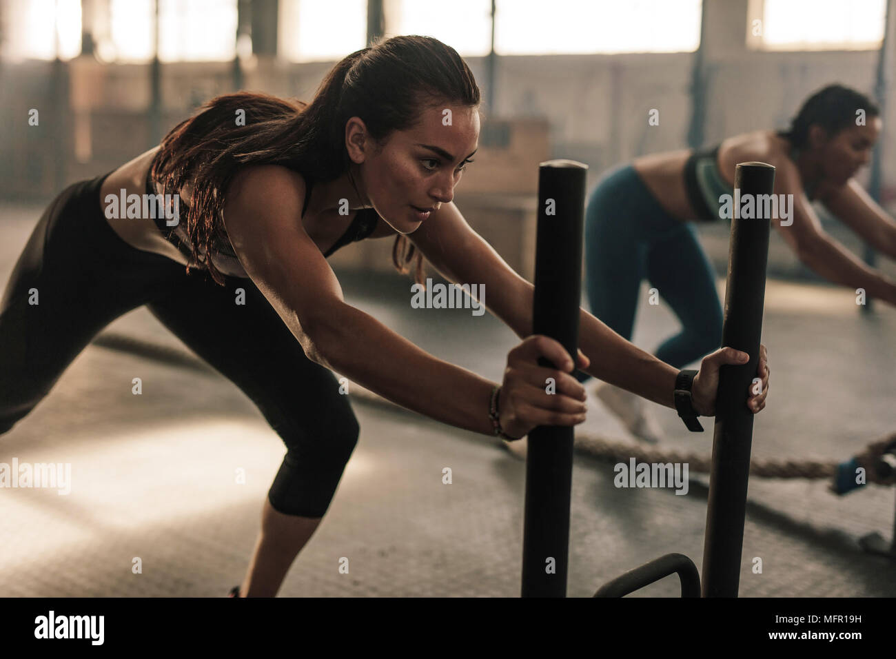 Strong young female pushing the prowler exercise equipment. Fit women exercising at gym. Stock Photo