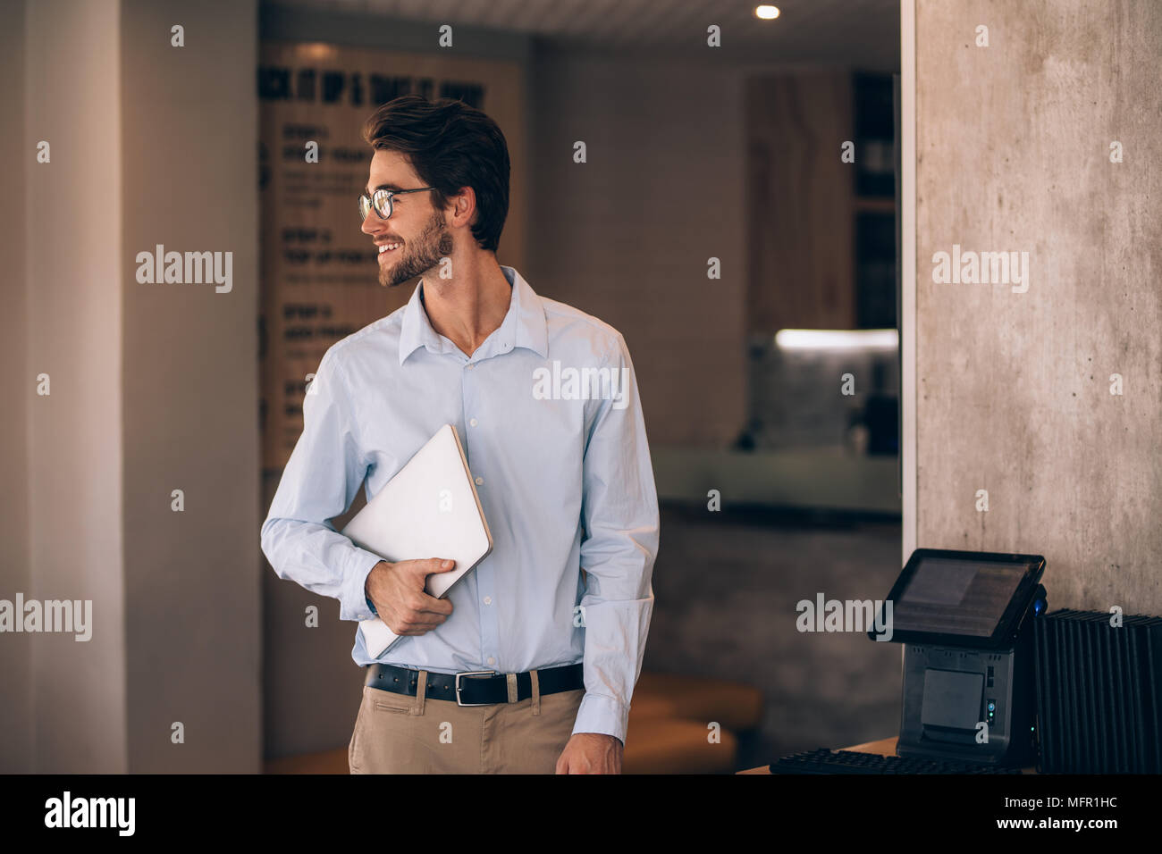 Young man standing in a cafe and looking away. Male restaurant manager with a laptop. Stock Photo