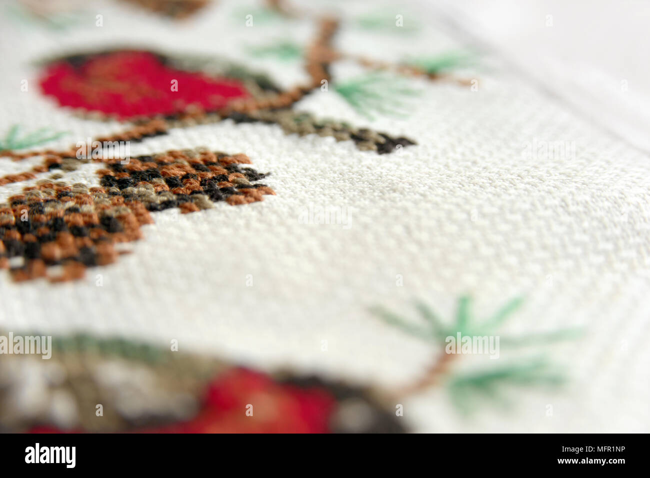 Cross-stitch embroidery. Red bullfinch on a fir-tree embroidery macro close up. View from above. Stock Photo