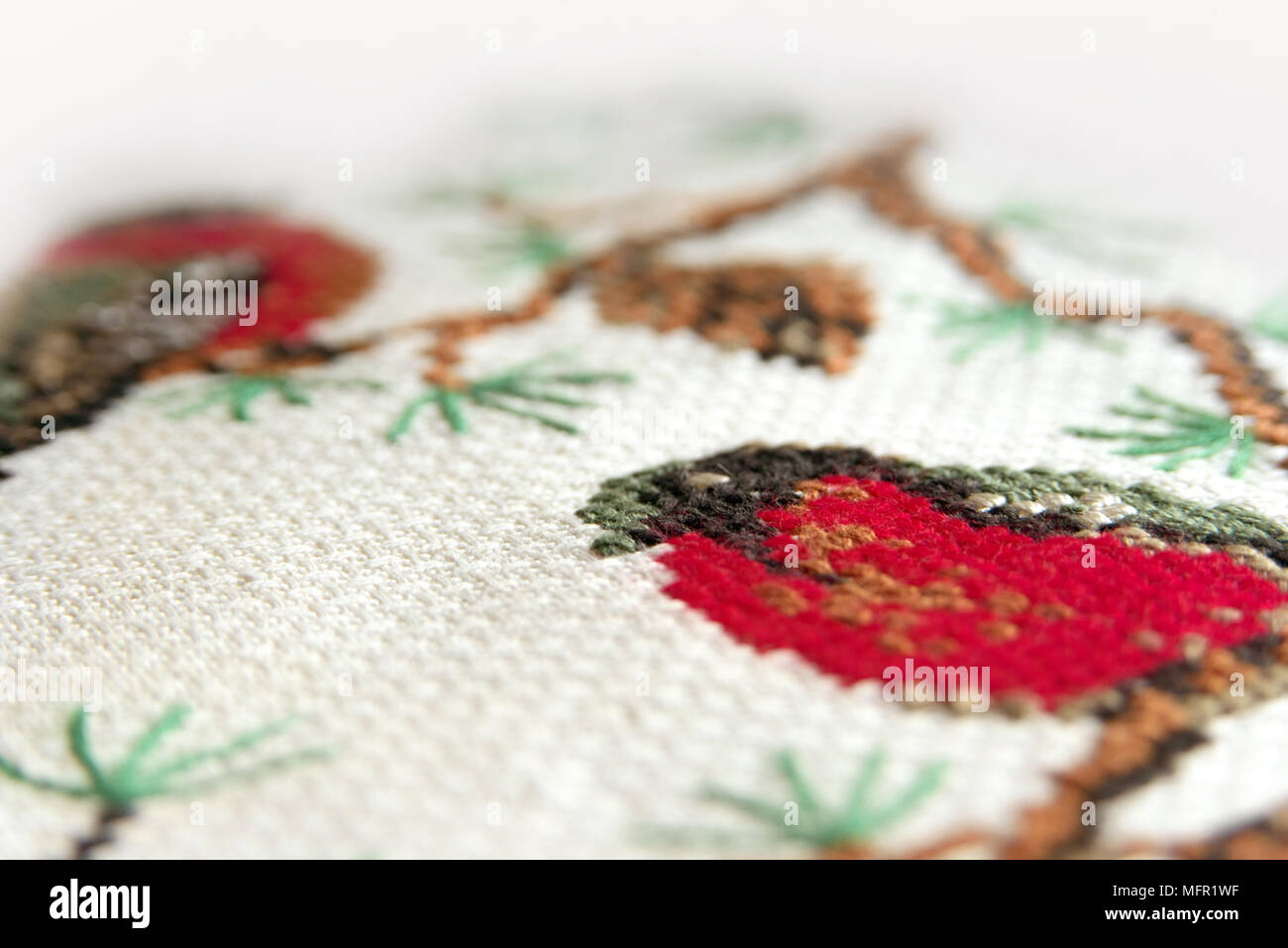 Cross-stitch embroidery. Red bullfinch on a fir-tree embroidery macro close up. View from above. Stock Photo