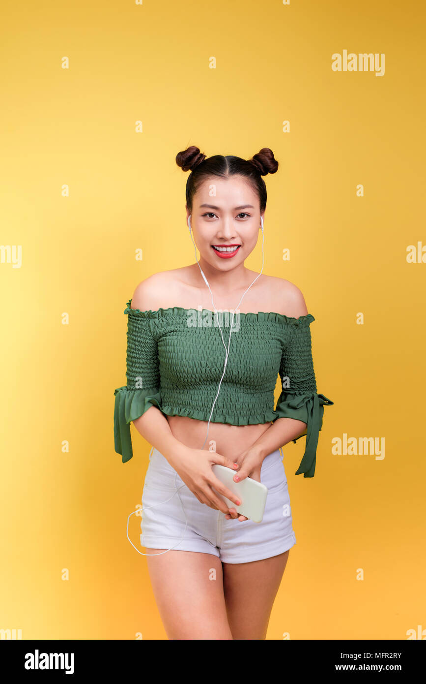 Fashion smiling asian woman listening to music in earphones over yellow ...