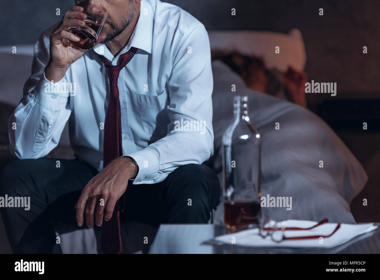 Man drinking whiskey in a suit while his woman is asleep Stock Photo