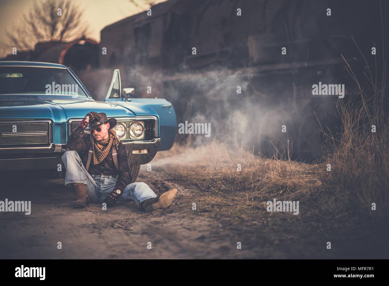 The American Cowboy Story. Caucasian Men Wearing Western Style Clothes and Cowboy Hat, Taking a Moment in Front of His American Classic Muscle Car. Ag Stock Photo