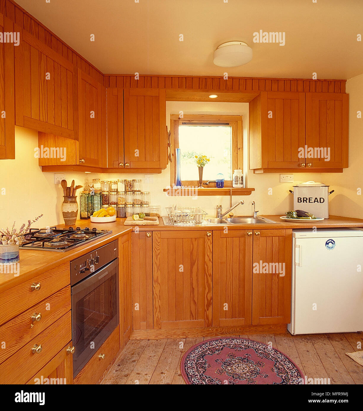 Country kitchen neutral walls wood units cooker hob white fridge sink unit kitchenwear bread bin window  hidden lit lighting ceiling light fitting woo Stock Photo