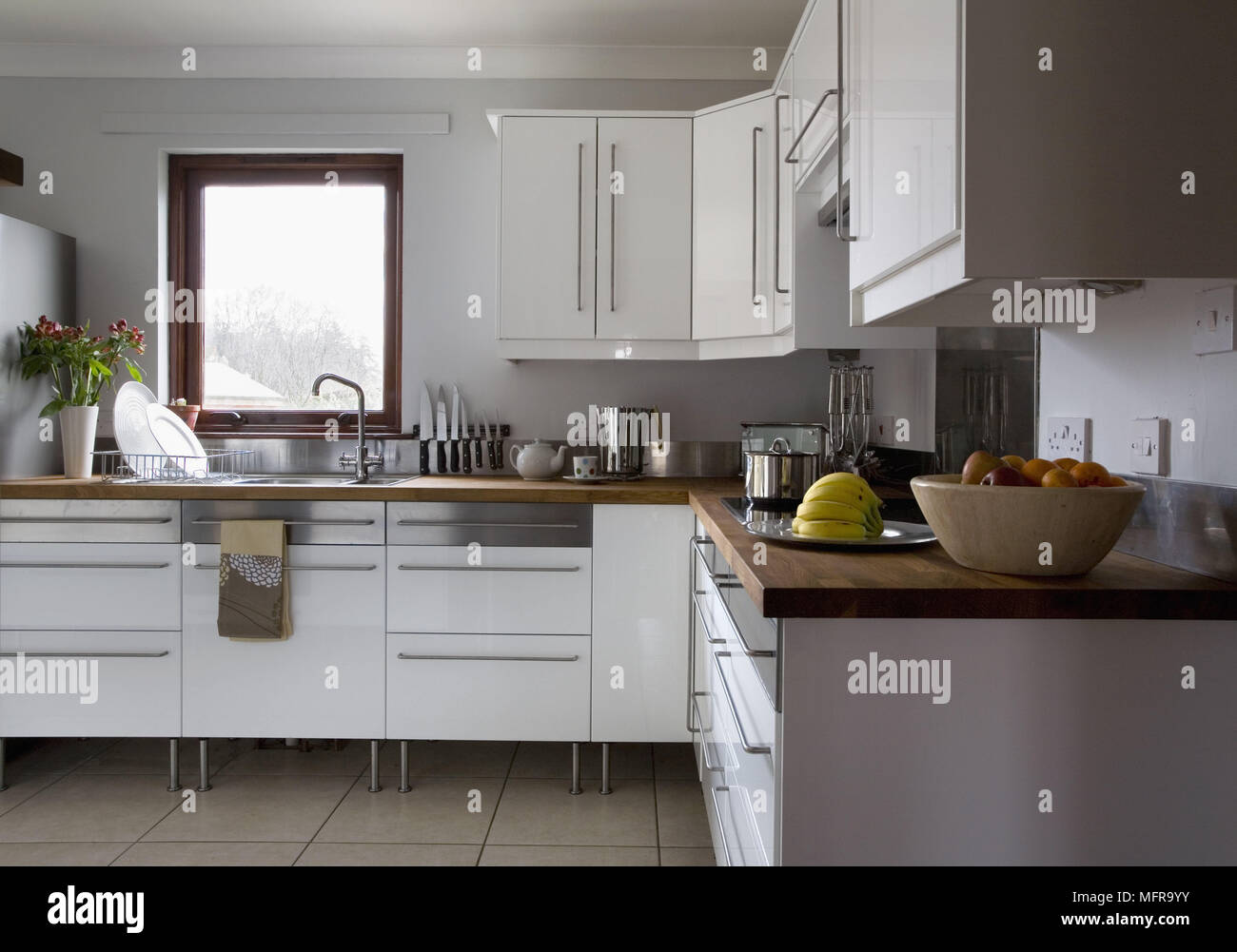 Modern kitchen with white units and sink beneath window Stock Photo - Alamy