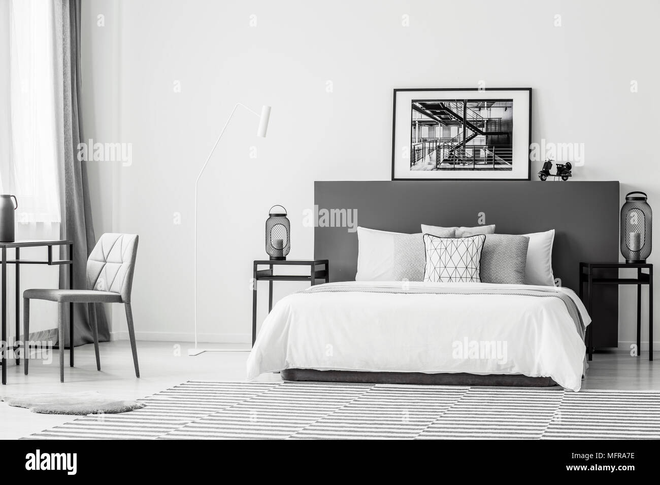 Grey chair at table near white bed in spacious contrast bedroom interior with black and white