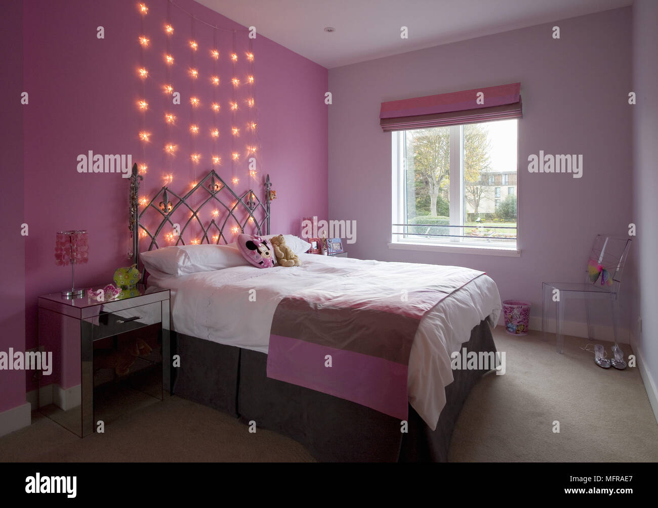Wrought iron double bed in pink bedroom with fairy lights on wall Stock Photo