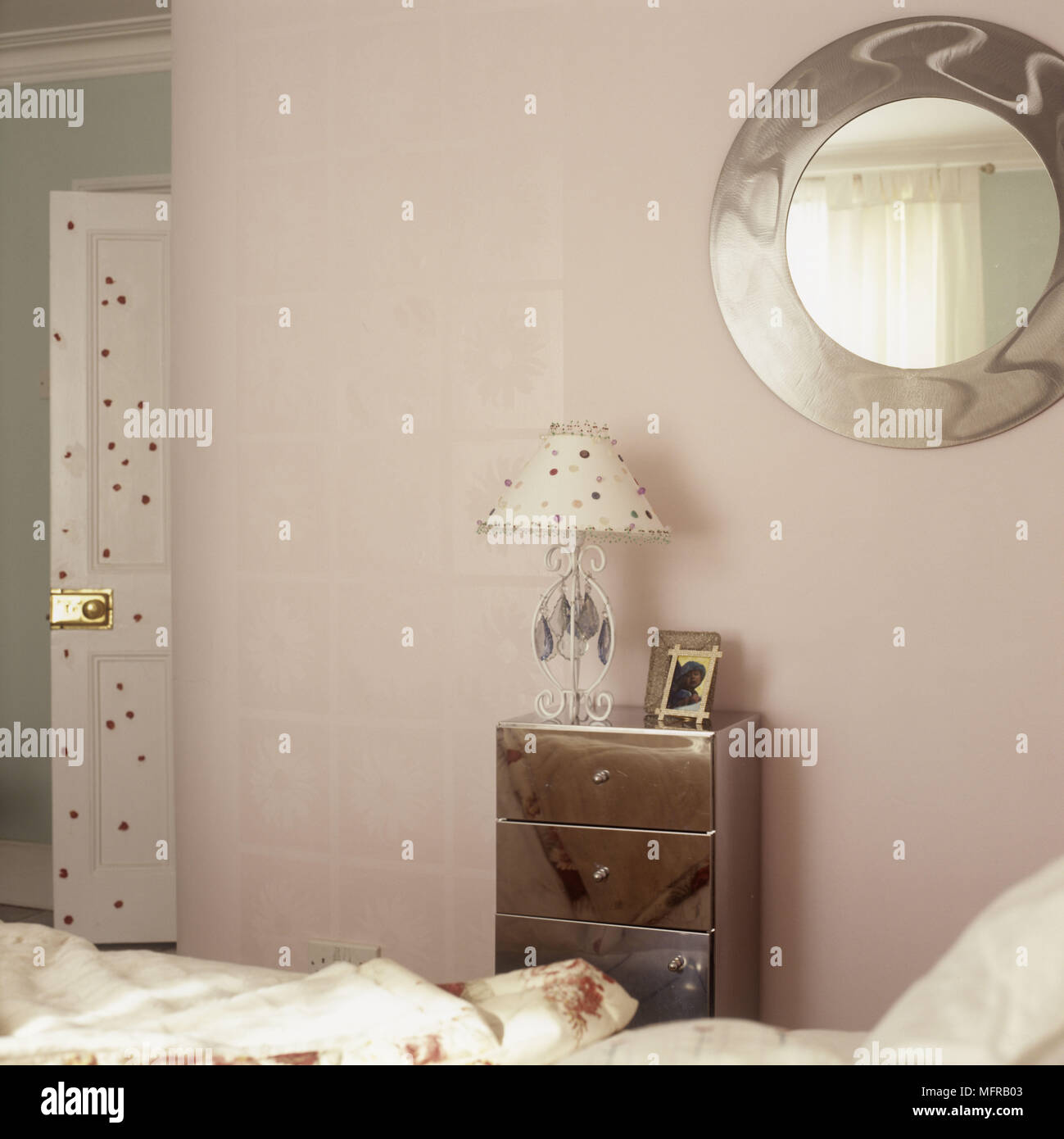 Pastel Coloured Bedroom With A Round Mirror And A Small Chest Of