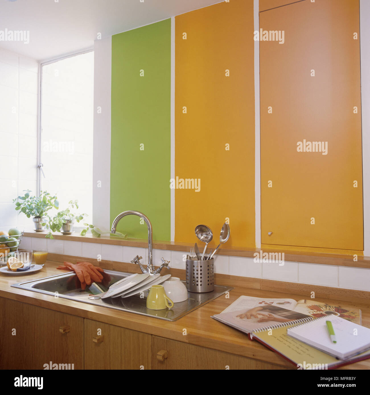 Wooden units with orange and green laminate cupboards clean dishes and recipe book Stock Photo