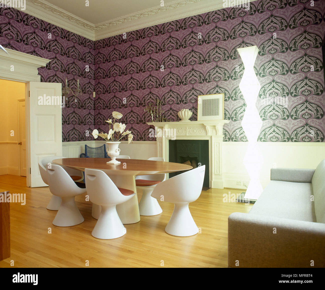 Modern Dining Room With Geometric Wallpaper Table Moulded Plastic Chairs Wood Floor And A Lit Sculptural Lamp Modern Dining Room With Geometric Wallpaper Table Moulded Plastic Chairs Wood Floor And A Lit Sculptural Lamp