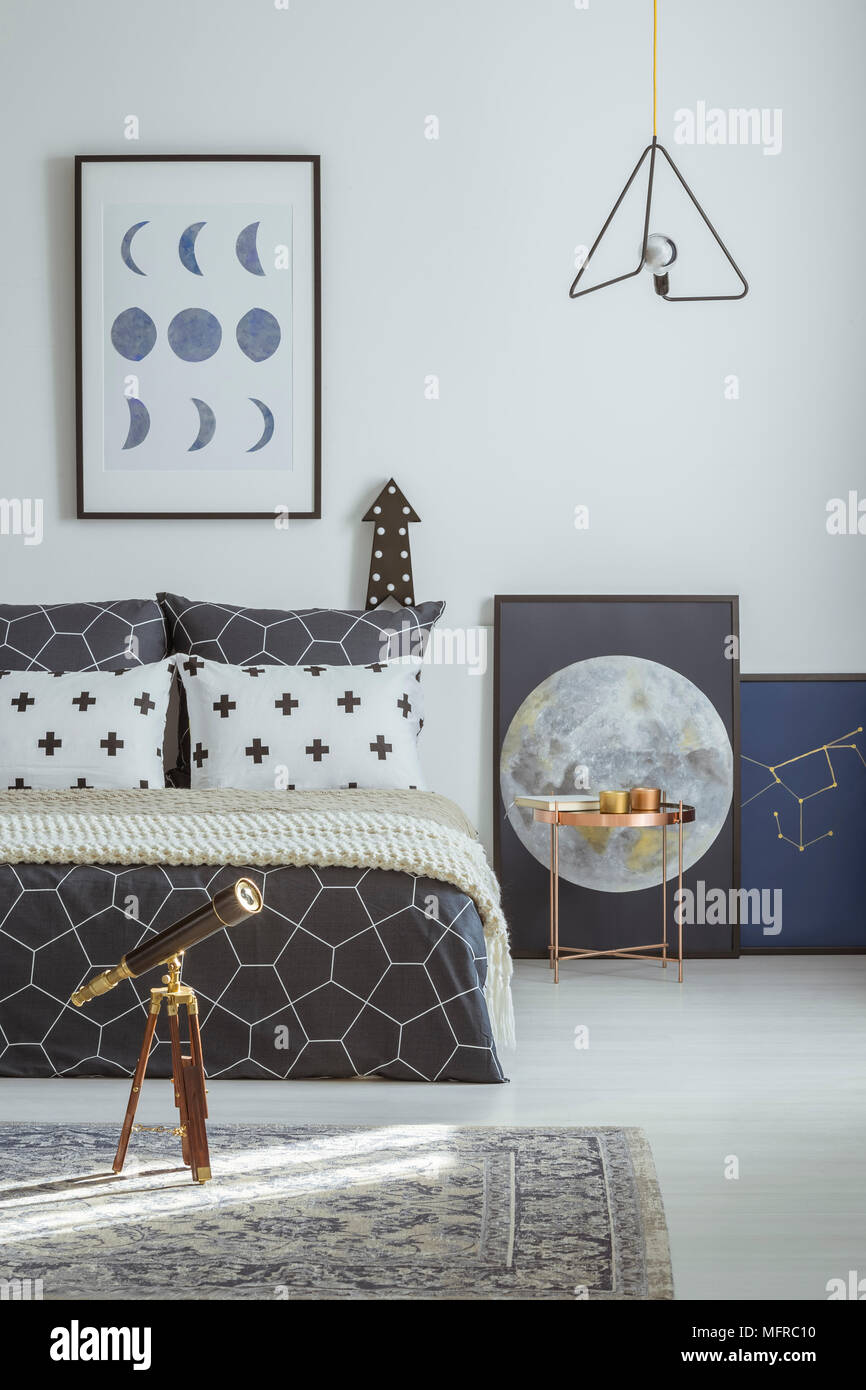 Telescope on patterned carpet and copper table next to bed in bedroom interior with moon poster Stock Photo