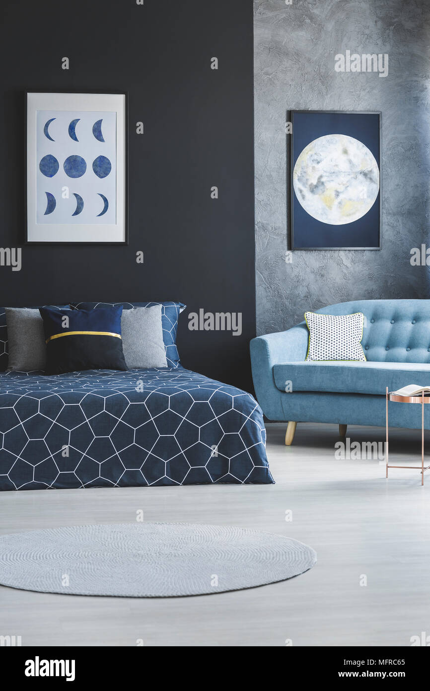 Blue sofa next to patterned bed in open space interior with moon poster