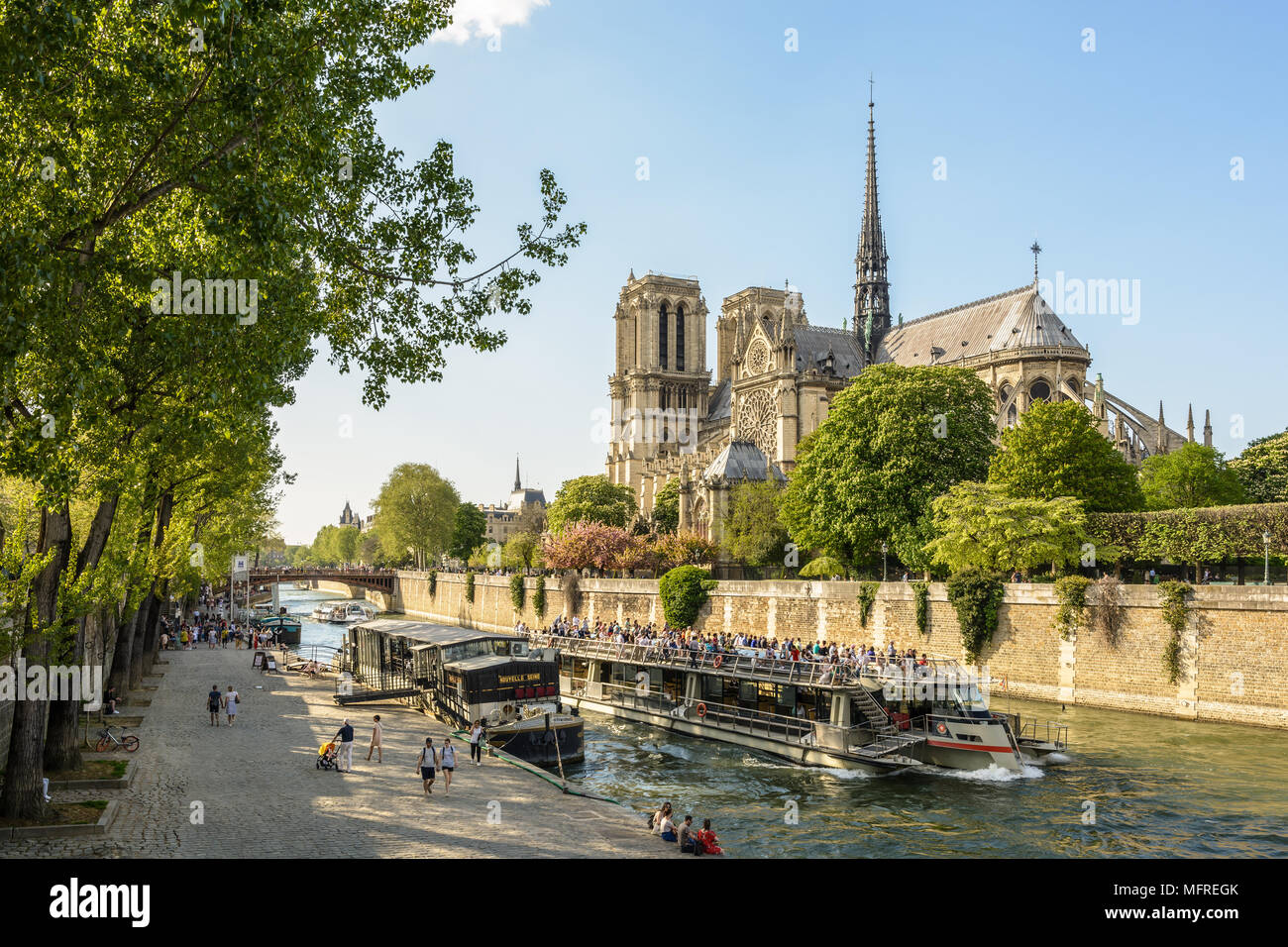 Parisians and tourists make the most of springtime to take a trip on a riverboat or stroll along the Seine in front of Notre-Dame de Paris cathedral. Stock Photo