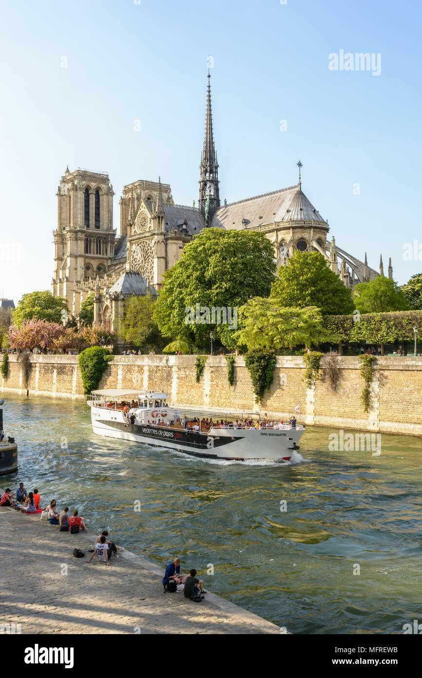 Parisians and tourists make the most of springtime to take a trip on a river boat or relax beside the Seine in front of Notre-Dame de Paris cathedral. Stock Photo