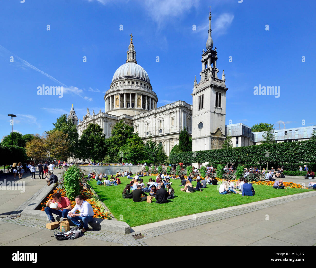 London, England, UK. People relaxing at lunchtime in Festival Gardens by St Paul's Cathedral. Tower of St Paul's Cathedral School (R) Stock Photo