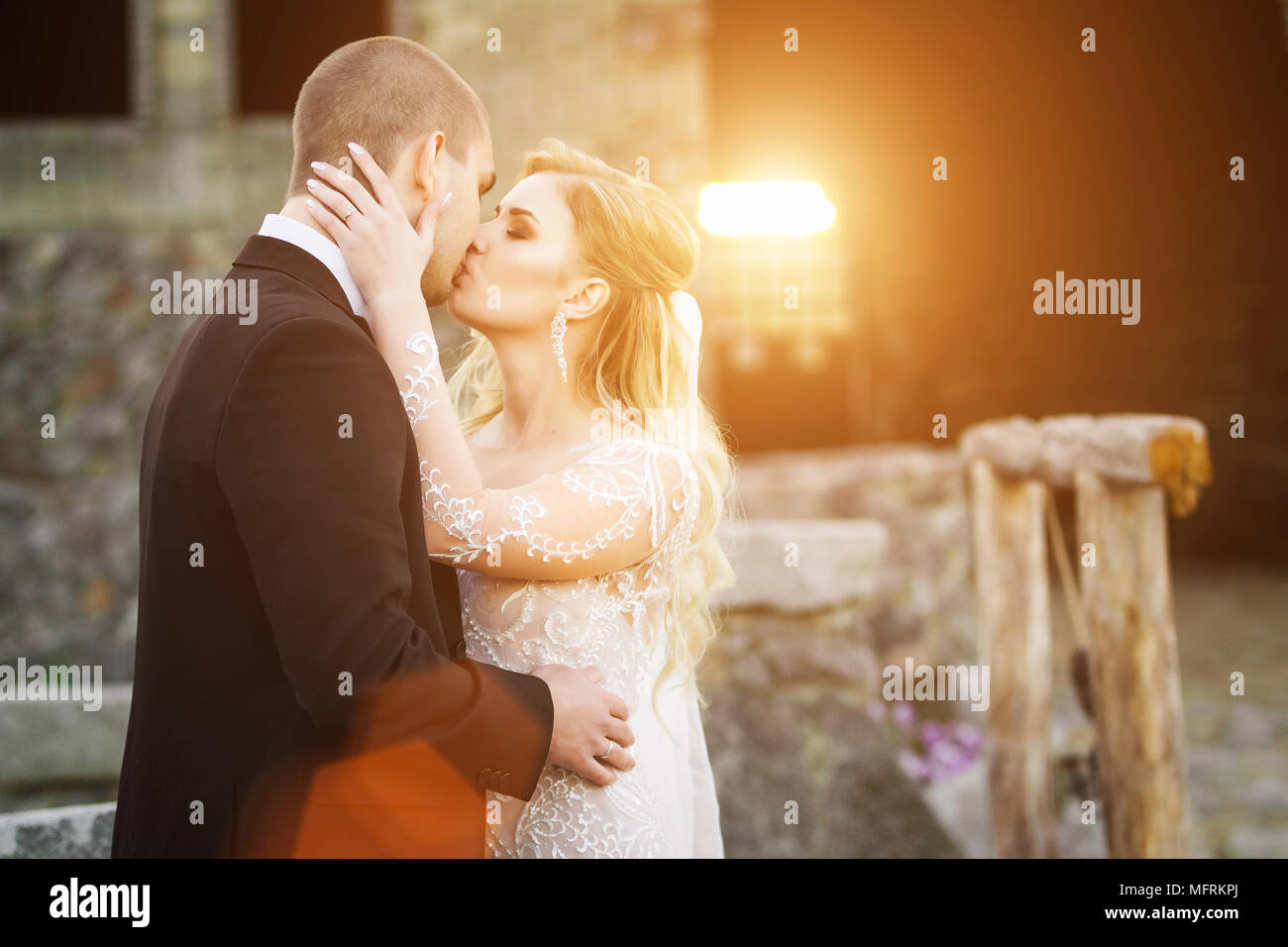 Bride and groom kissing near the lightened by sunset building Stock ...
