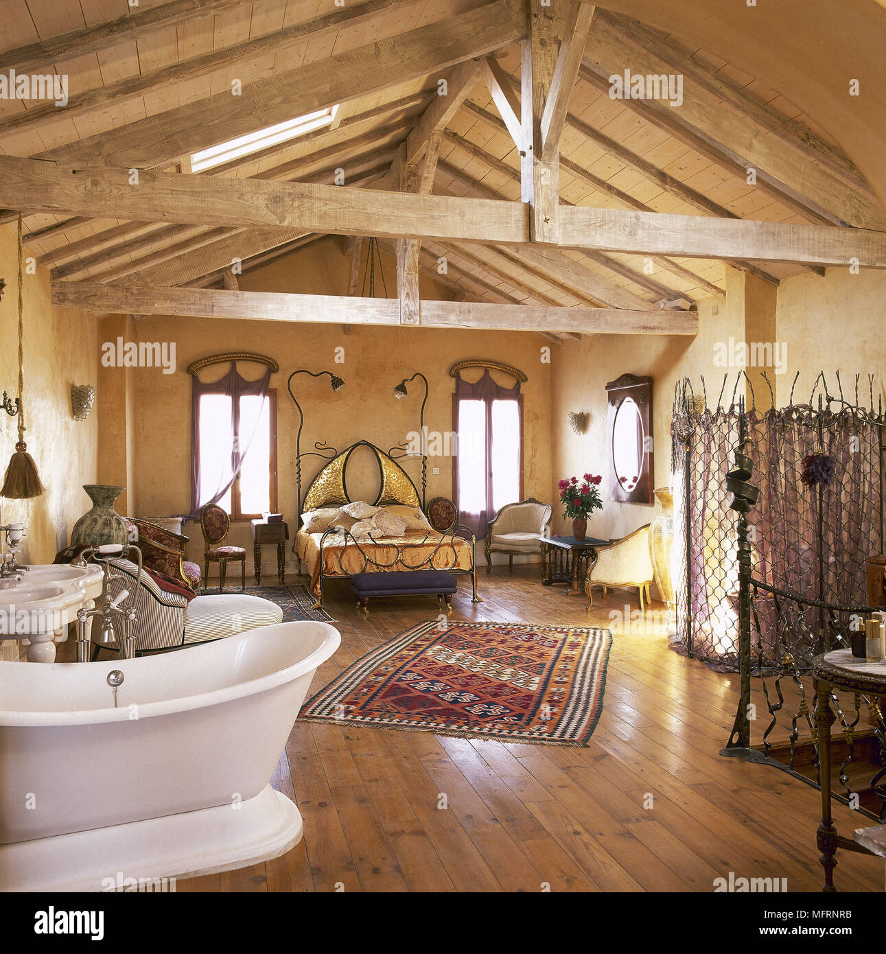 Country style open plan bedroom with beamed roof  and wood floor with freestanding roll top bathtub Stock Photo