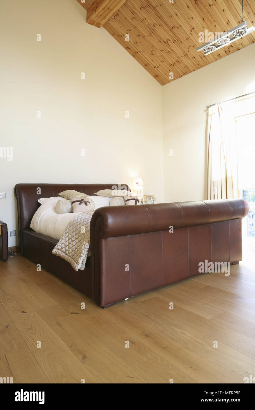 Upholstered leather double bed in spacious bedroom with high timber ceiling Stock Photo