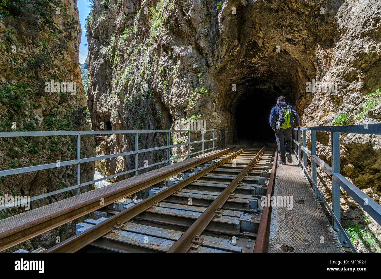 Hiking at Vouraikos gorge following the Diakopto–Kalavrita rack railway route. Peloponnese - Greece. A man with backpack is entering a tunnel Stock Photo