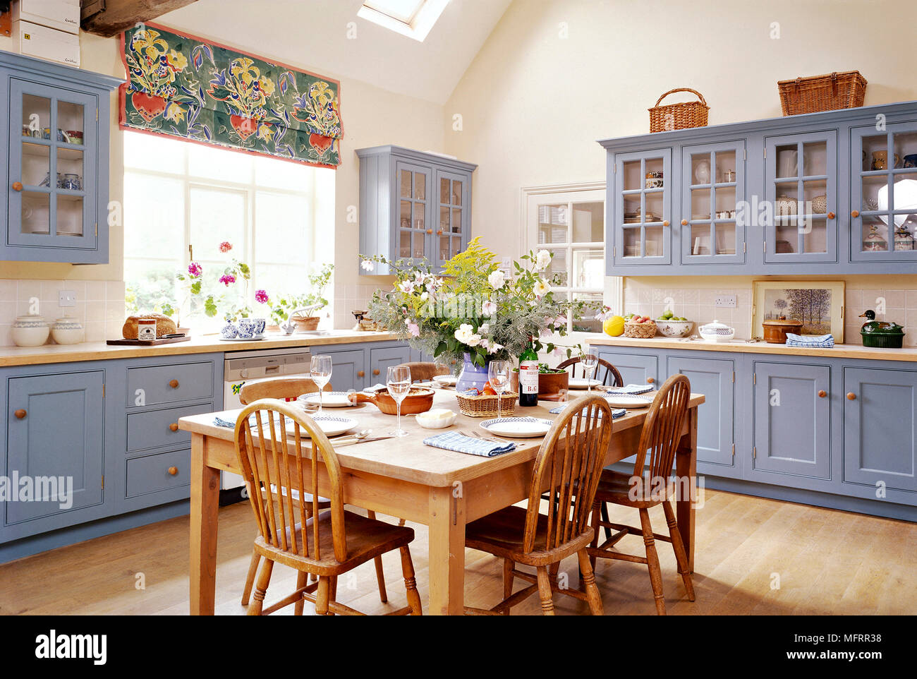 A country kitchen with blue cupboards, wooden table and chairs, wooden floor, set table, flower arrangement, Stock Photo