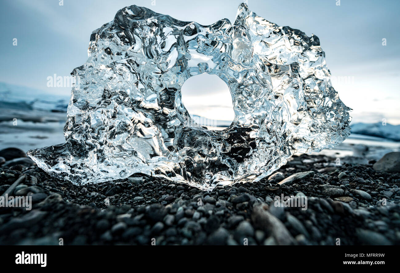 Ice, ice chunks with hole at the black gravel beach, glacier lagoon Jökulsárlón, glacier lake, southern edge of Vatnajökull Stock Photo