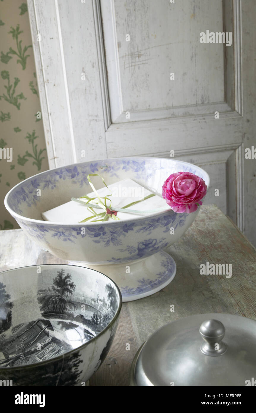 Country kitchen detail with distressed wooden door floral wallpaper and china bowl containing gift. Stock Photo
