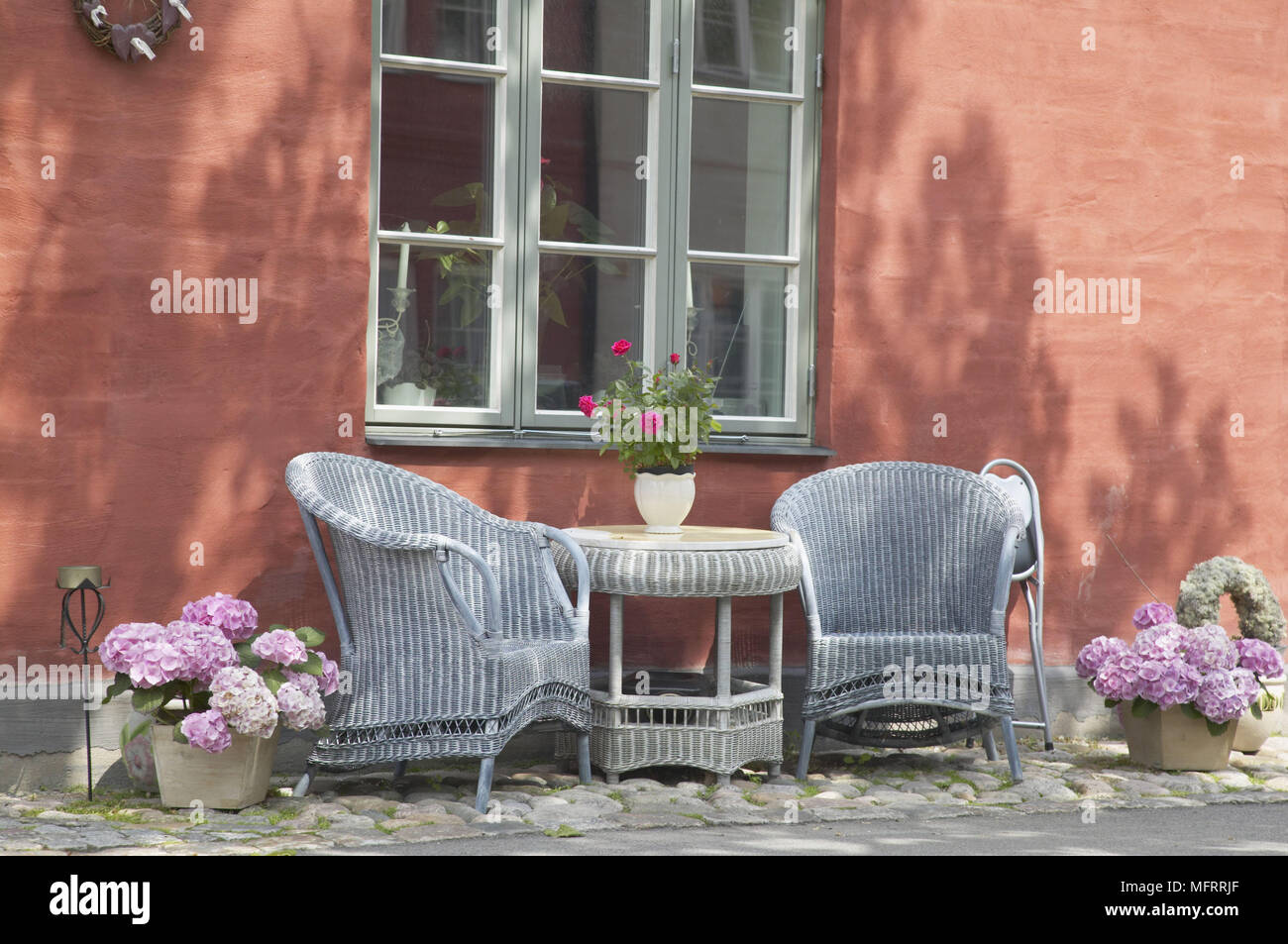 Two blue wicker chairs and a table and flowers by window Stock Photo