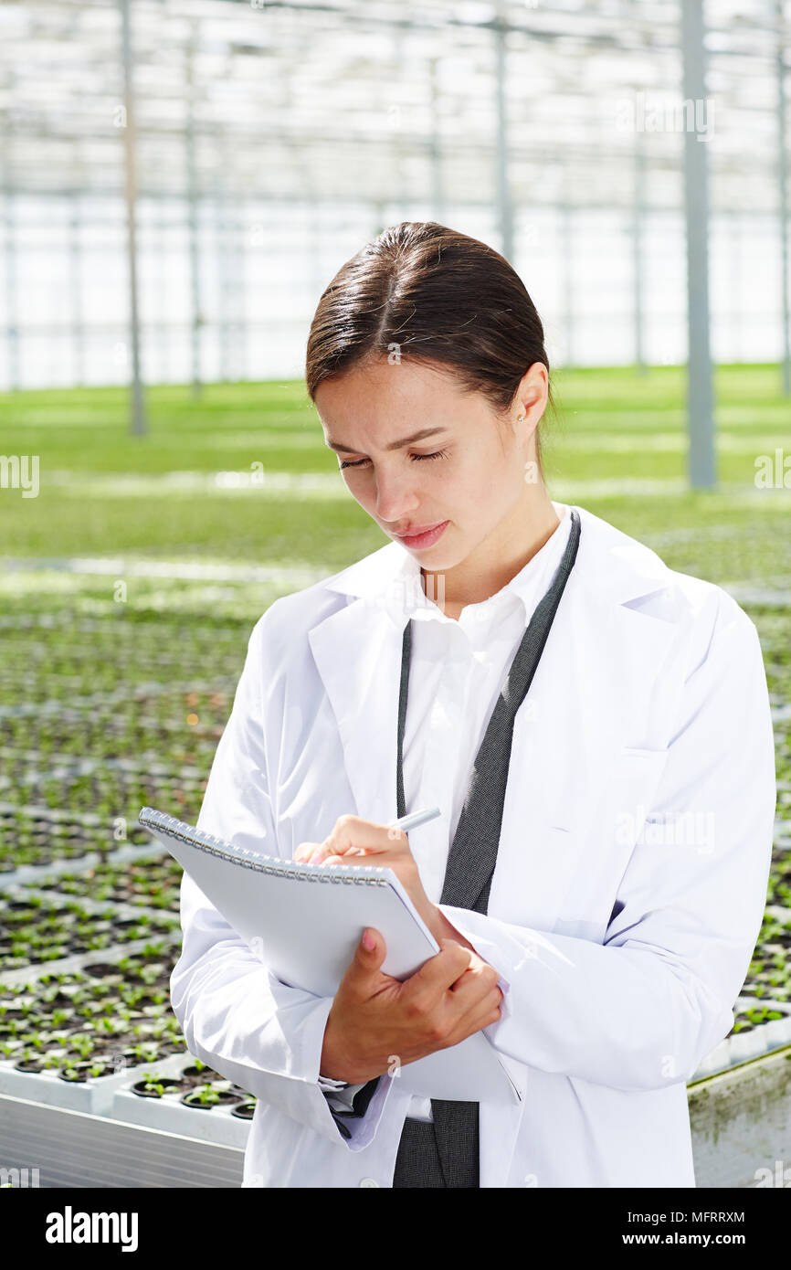 Young attractive female agricultural engineer in white overall making