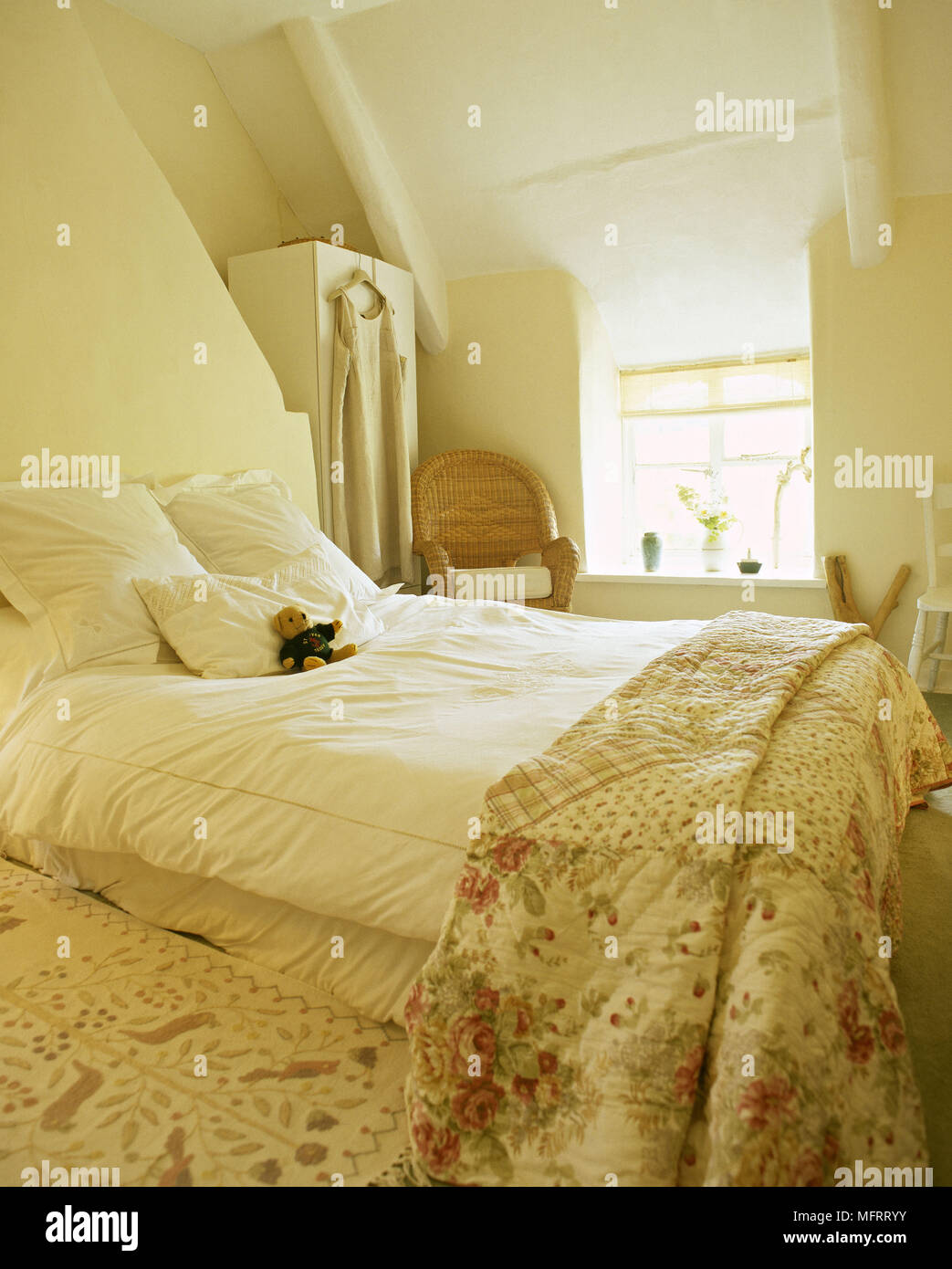 Country yellow bedroom with sloping ceiling floral coverlet and a sunny window. Stock Photo