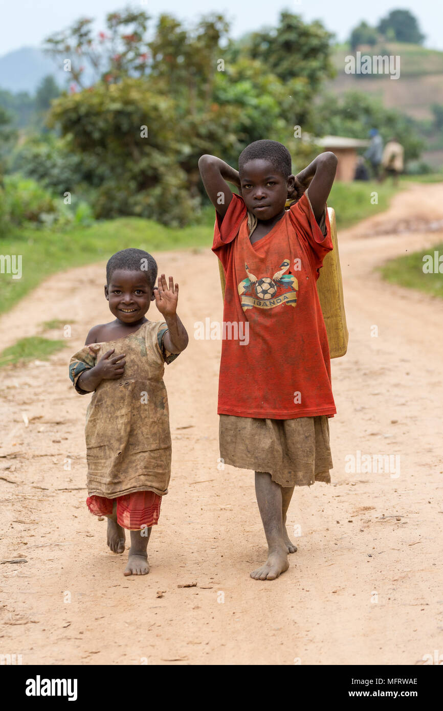 Two African children on a sandy track, waving, near Lake Mutanda, Uganda Stock Photo