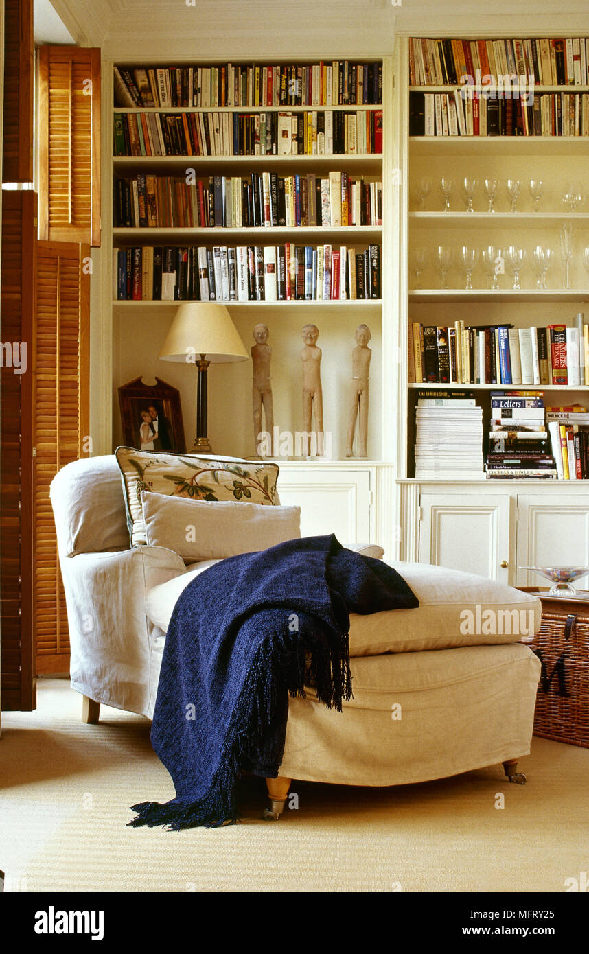 Modern, carpeted sitting room with a slipcovered chaise longue, shuttered windows, and a wall