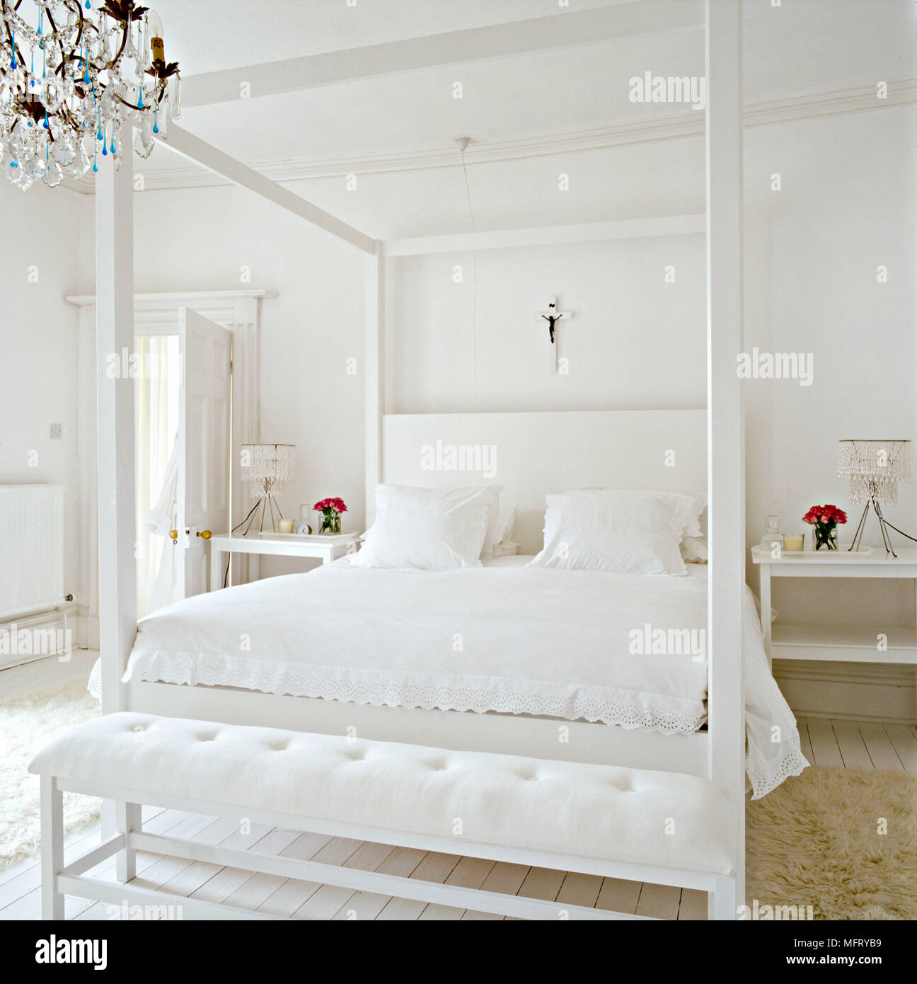 A modern minimalist white bedroom with double four poster bed with upholstered headboard bench seat bedside tables Stock Photo