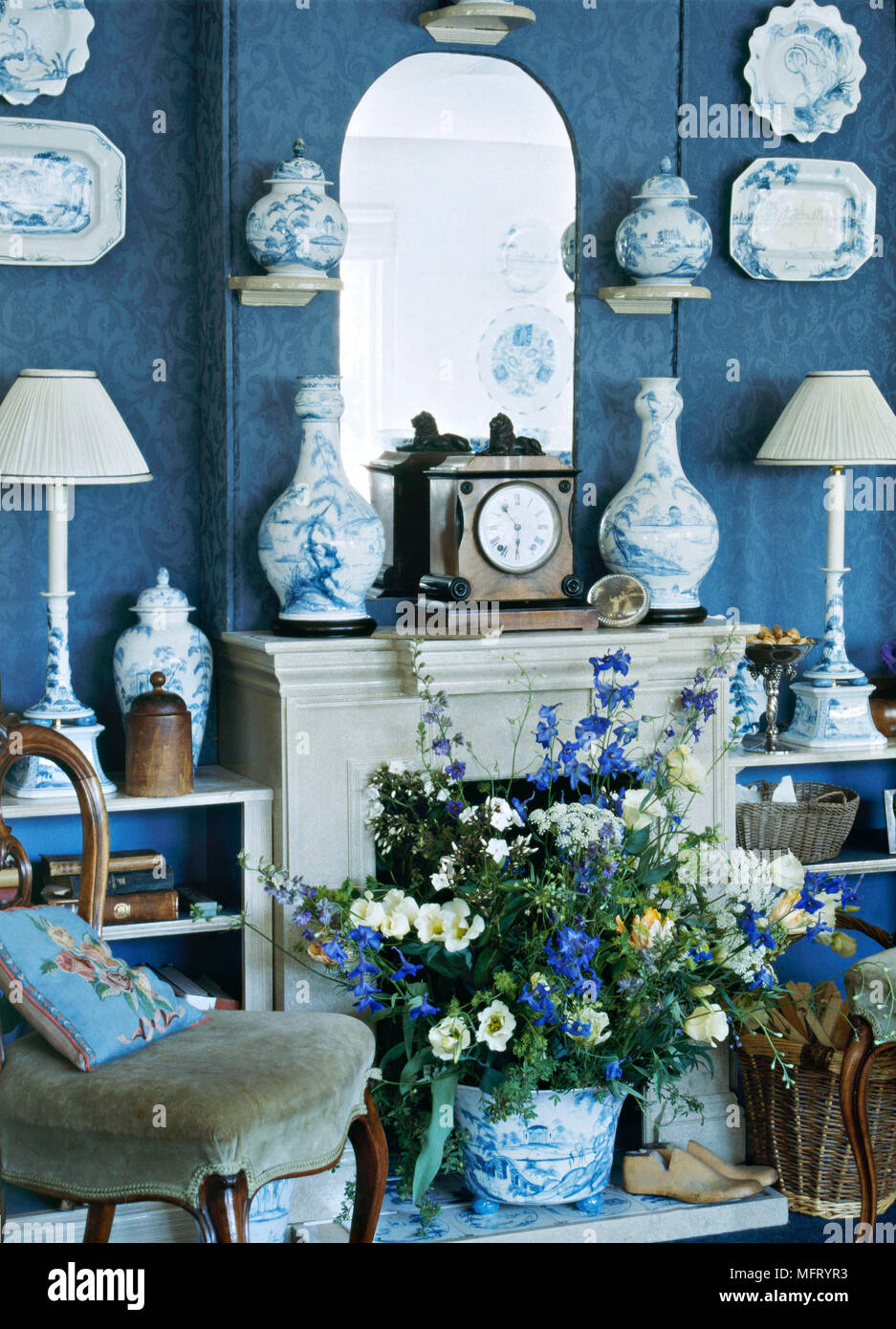 Sitting room fireplace blue wallpapered walls chair flower arrangement in fireplace clock  interiors rooms blue white china pair of lamps china on wal Stock Photo