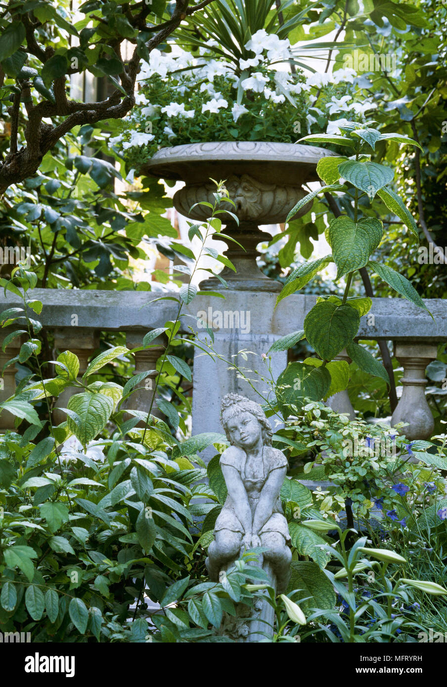 Stone urn planter on stone wall small statue of girl set amongst shrubs; planters statuettes figures focal points foliage Stock Photo