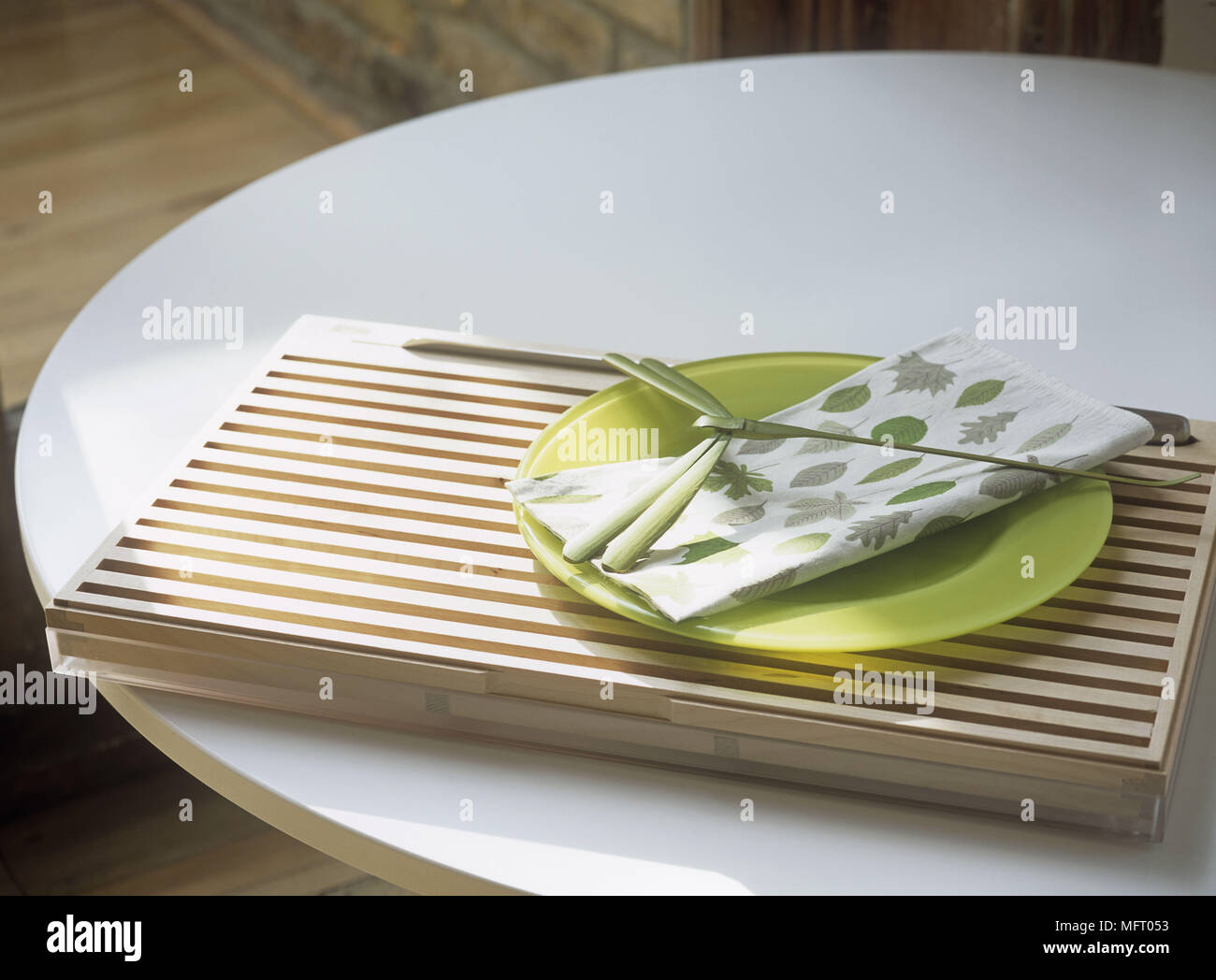 White circular table with wooden tray green plate and napkin with leaf motif and palm frond on top Stock Photo