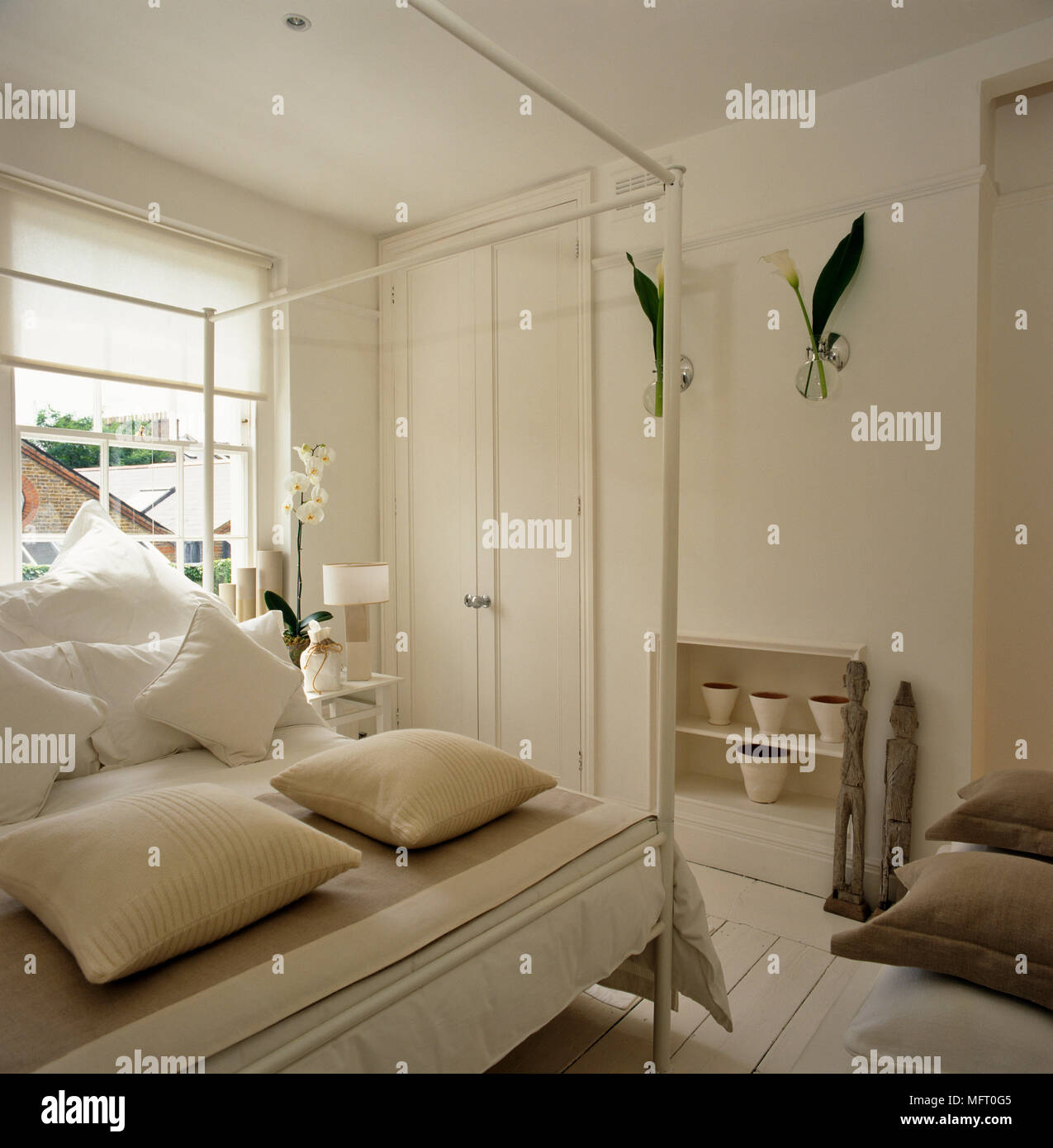 White bedroom with four poster bed and cushions on painted floorboards