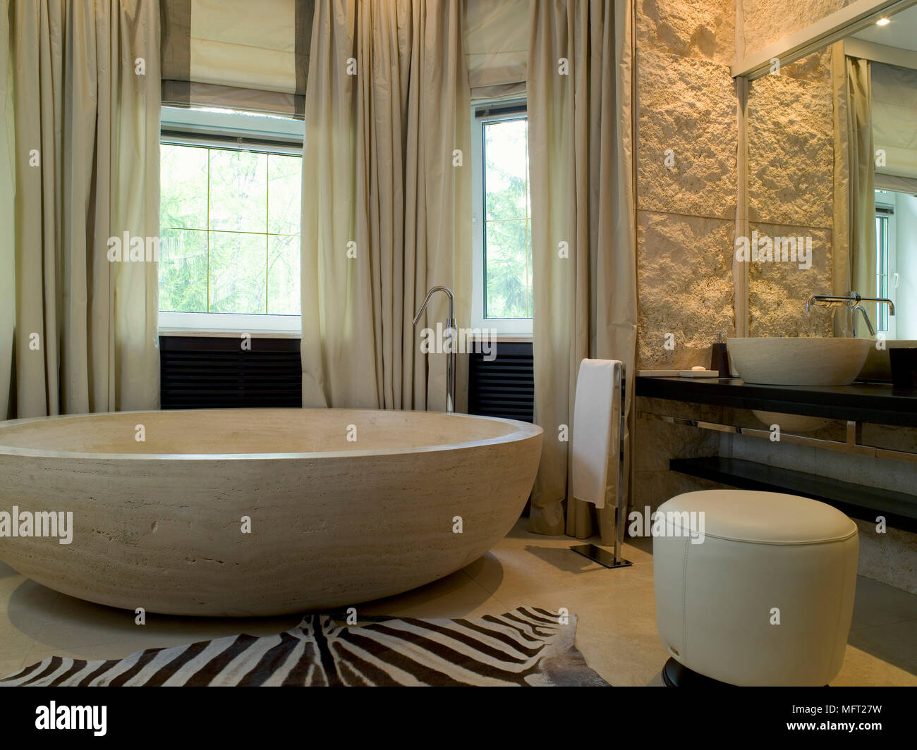 Luxurious bathroom with large circular bathtub next to animal print carpet and large mirror above wash basin Stock Photo