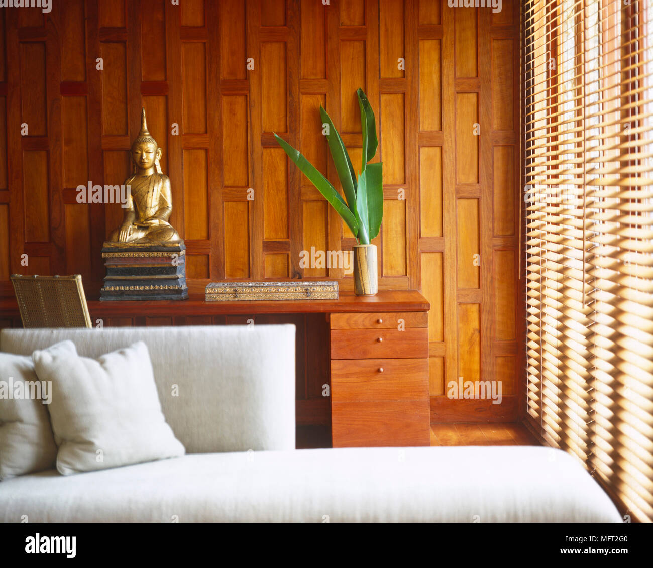 Buddha statue on desk with drawers against wood panelled wall Stock