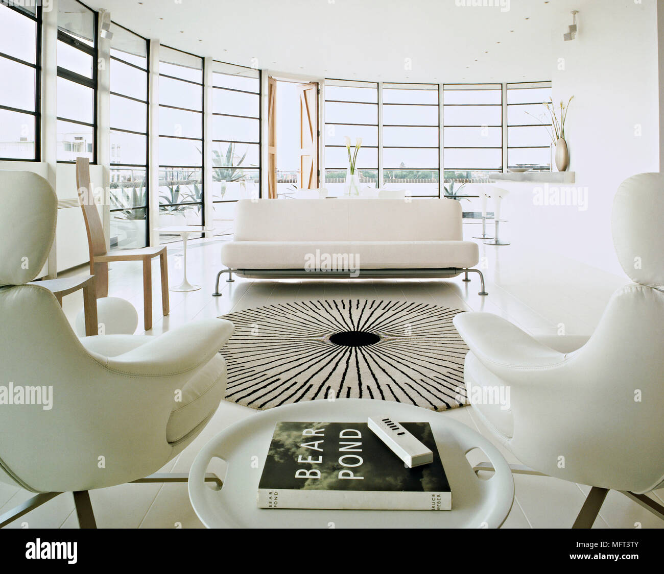 An ultra modern minimalist sitting room with curving glass walls  upholstered sofa and armchairs rug Stock Photo - Alamy, image size:1300x1125