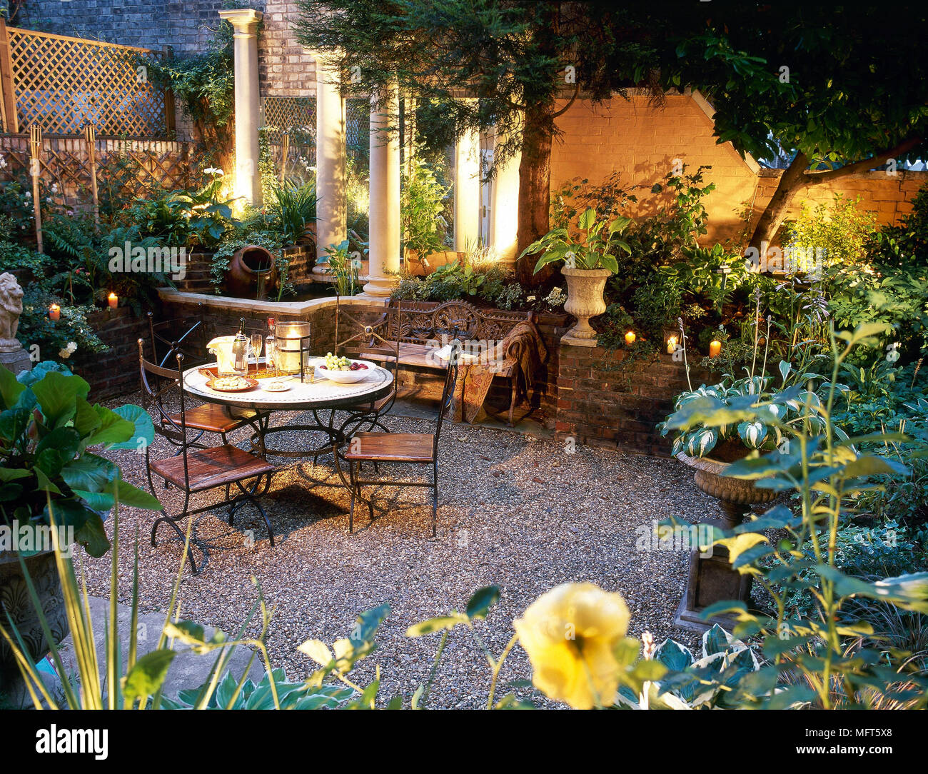 A courtyard, town garden with gravel patio area, lit in the evening, table and chairs, table setting for two, Stock Photo
