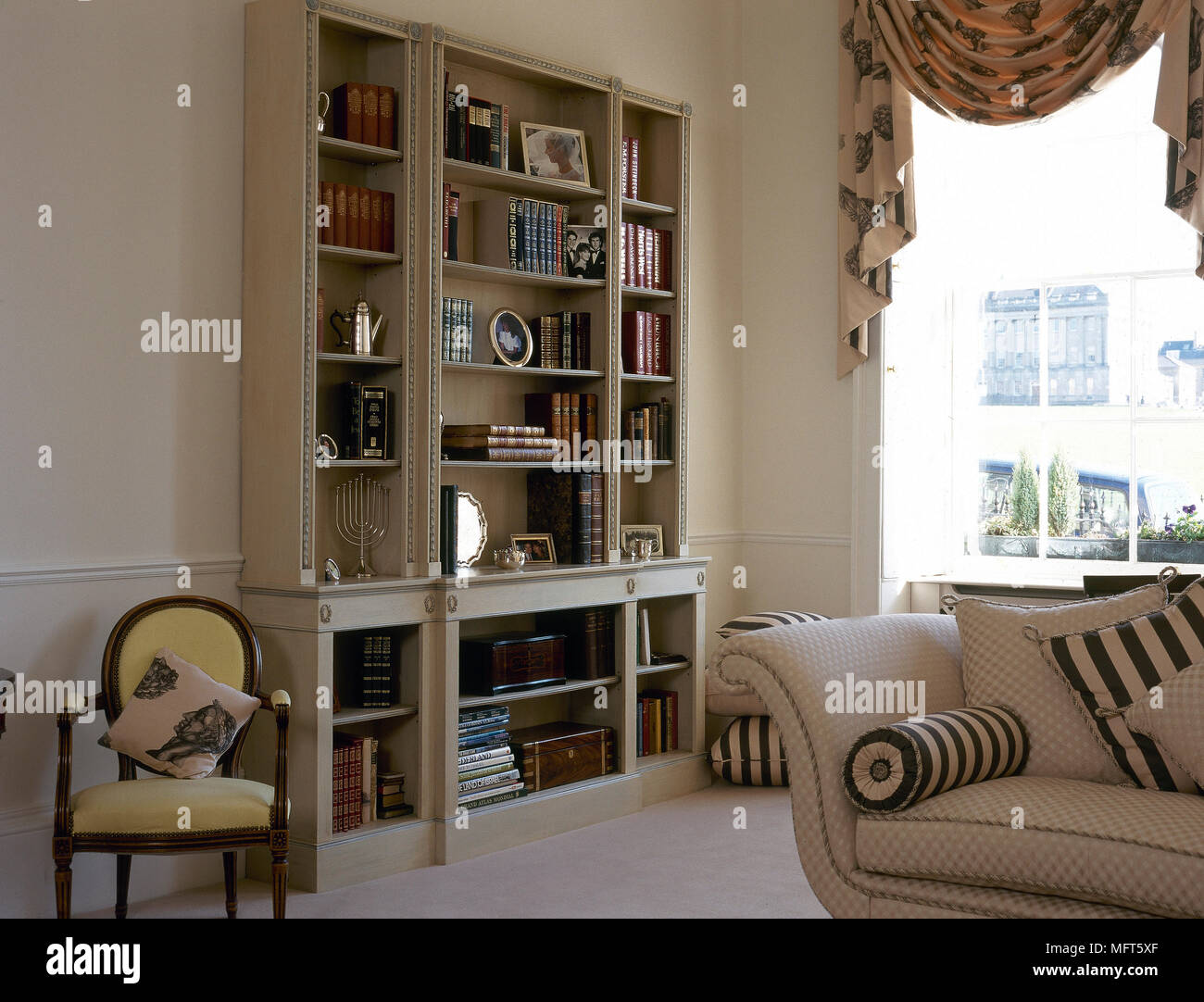 A traditional, neutral sitting room with bookcase, swag curtains, sofa, period chair, Stock Photo