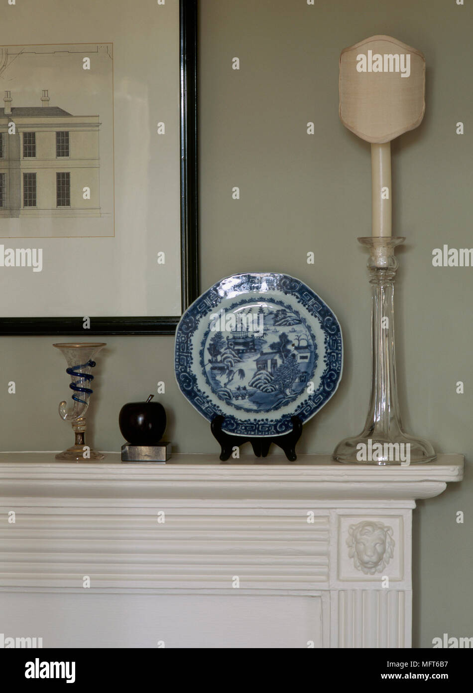 A detail of a traditional fireplace mantelpiece, a glass candlestick and blue white china plate Stock Photo