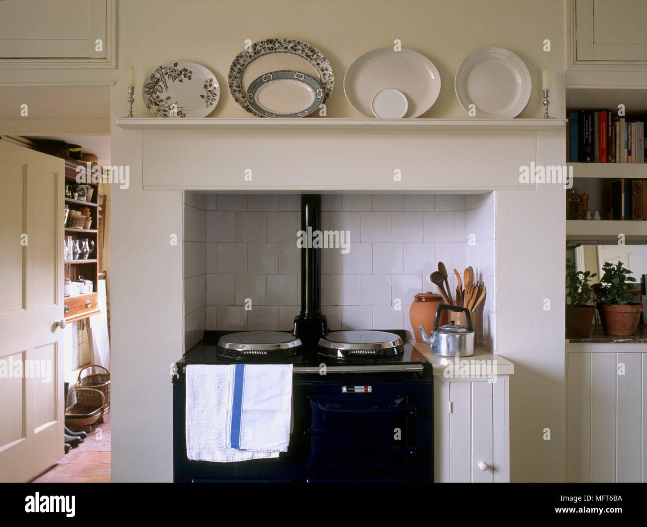 A detail of a traditional country kitchen, a black Aga range set in tiled recess, ceramic plates