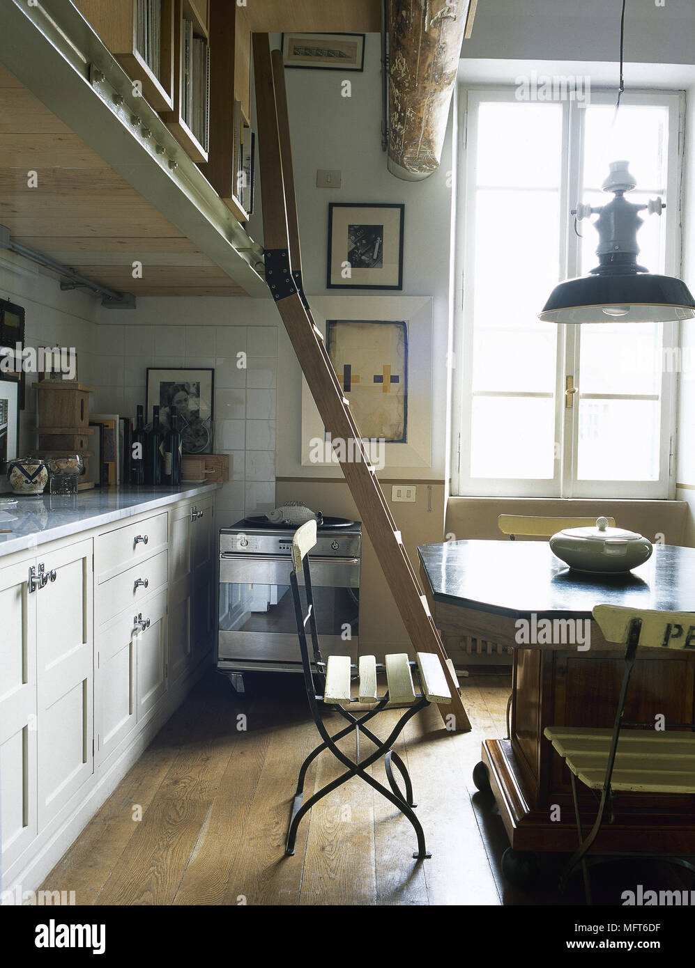 Dining table and chairs in open plan room with ladder to upper gallery floor Stock Photo