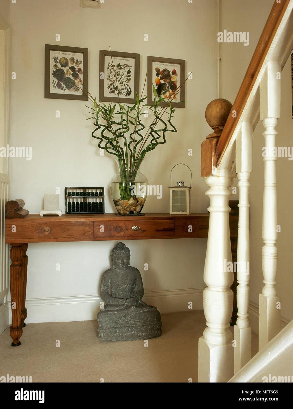Traditional stairway landing with a newel post, framed botanical artwork, buddha statue, and a wooden table. Stock Photo