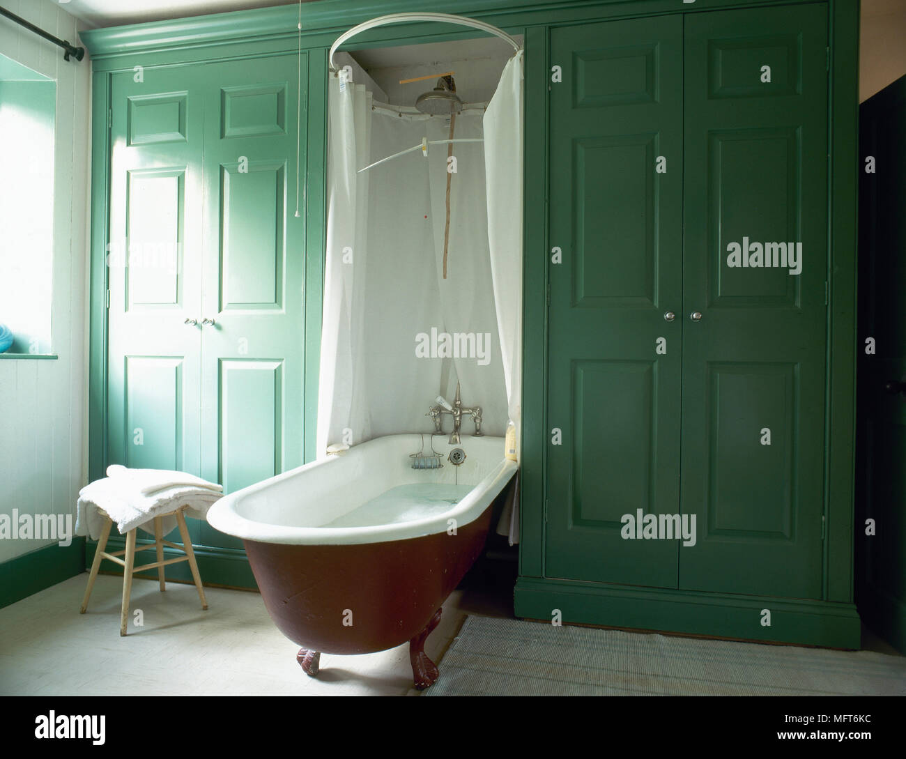 Traditional Bathroom With Built-In Cupboards, Free Standing Roll Top Bathtub,  And A Canopy Shower Curtain Stock Photo - Alamy