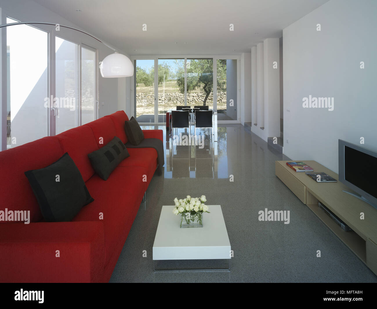 Red sofa facing television on unit in modern open plan sitting room with dining area Stock Photo