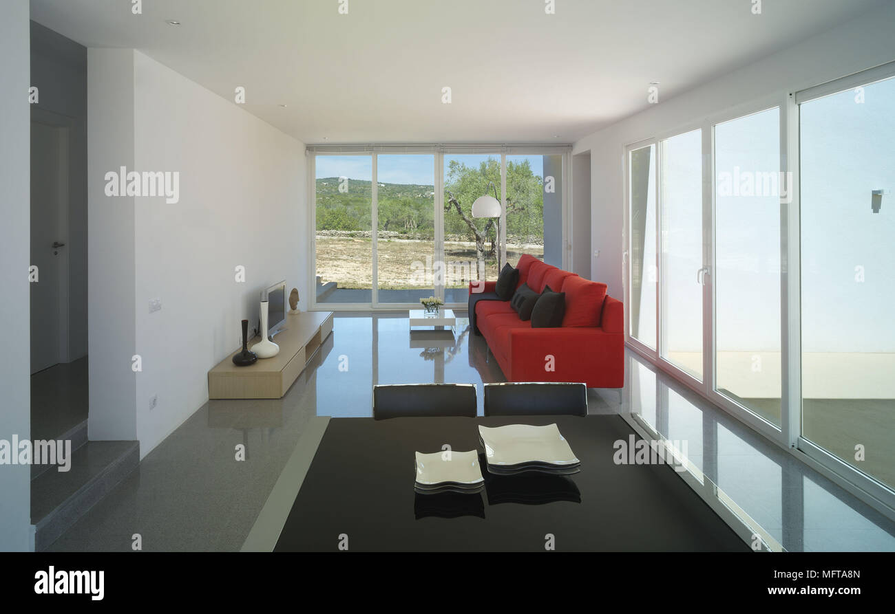 Red sofa facing television on unit in modern open plan sitting room with dining area Stock Photo